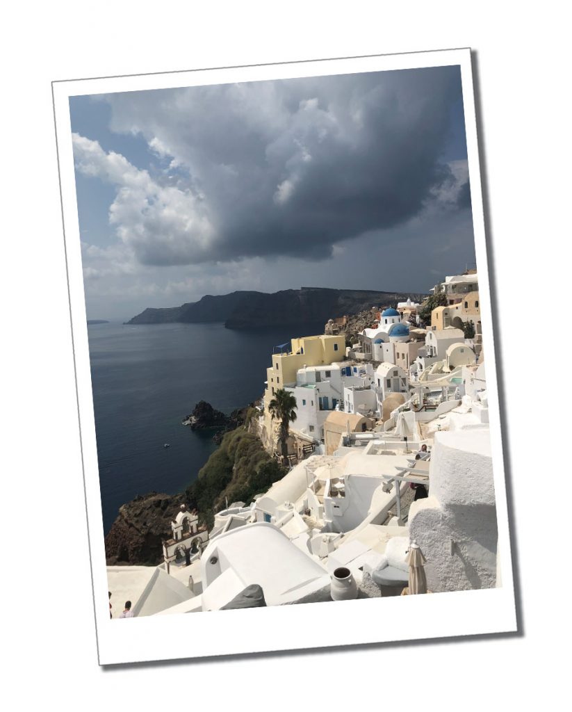 Slate grey skies with a hint of sunlight over the beautiful panorama of Santorini's whitewashed buildings that cling to the hillside overlooking the bay.