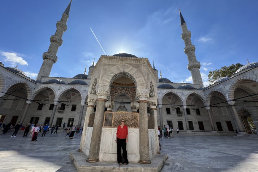A blonde woman standing in the courtyard of a mosque on a sunny day